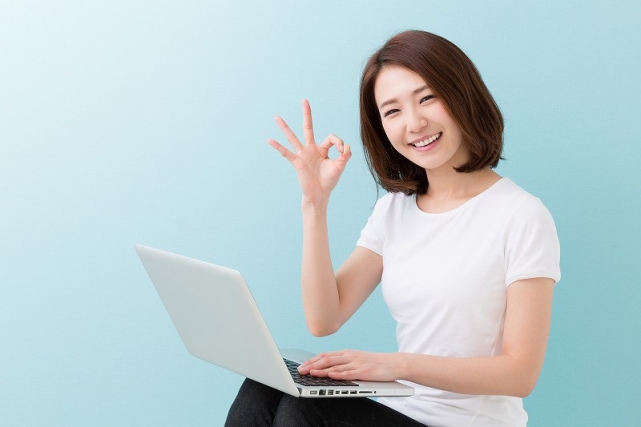 笑顔の女性がノートパソコンを操作しながらOKサインを出している